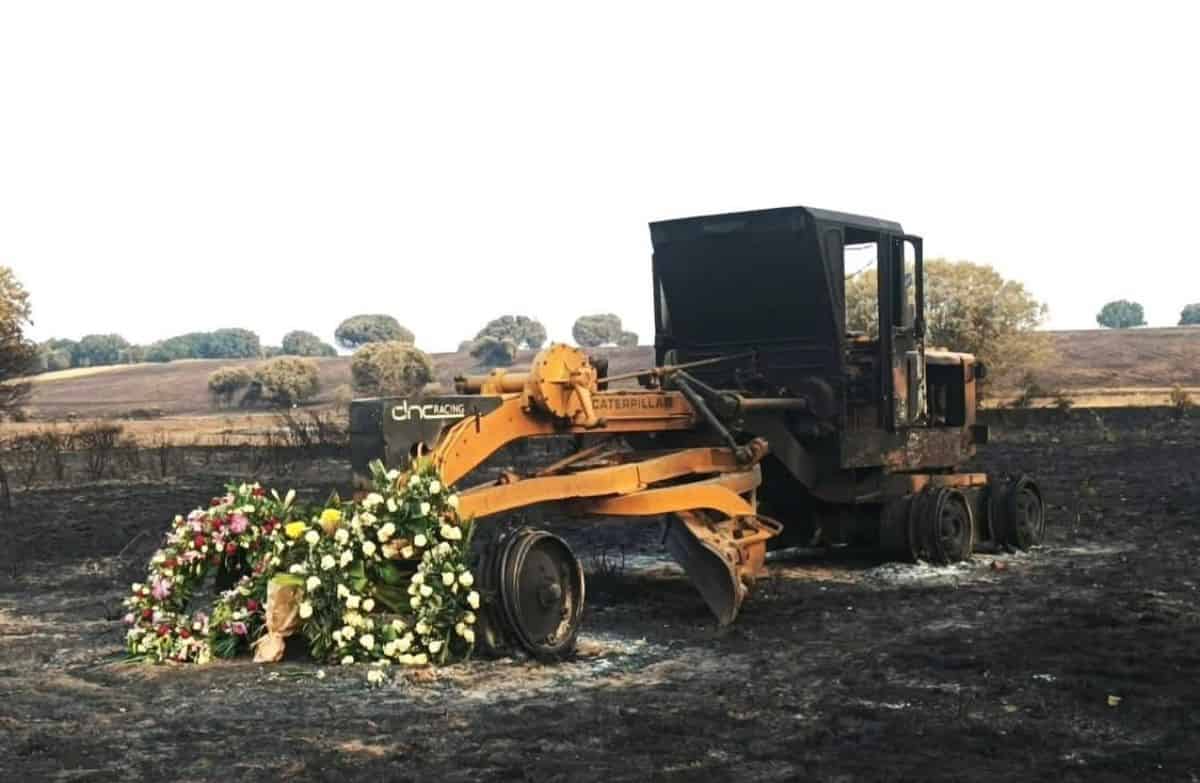 Vehículo pesado quemado con homenaje floral en un paisaje rural, maquinaria de construcción destruida, símbolo de pérdida y recuerdo